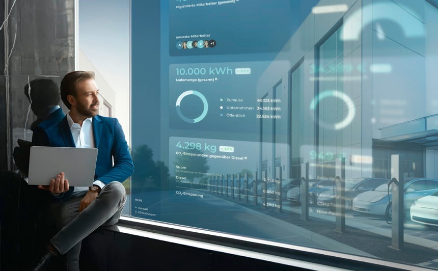 Geschäftsmann mit Laptop sitzt vor Panoramafenster mit Daten-Dashboard – Visualisierung von Datenanalysen und E-Mobility-Strategie für OEMs