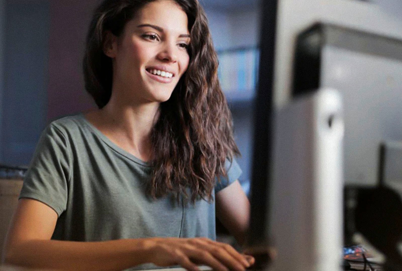 Junge Frau sitzt lächelnd am Schreibtisch und nutzt den e-mobilio Shop am Computer, um Produkte rund ums Laden wie Wallboxen und Zubehör für Ihren E-Dienstwagen zu bestellen