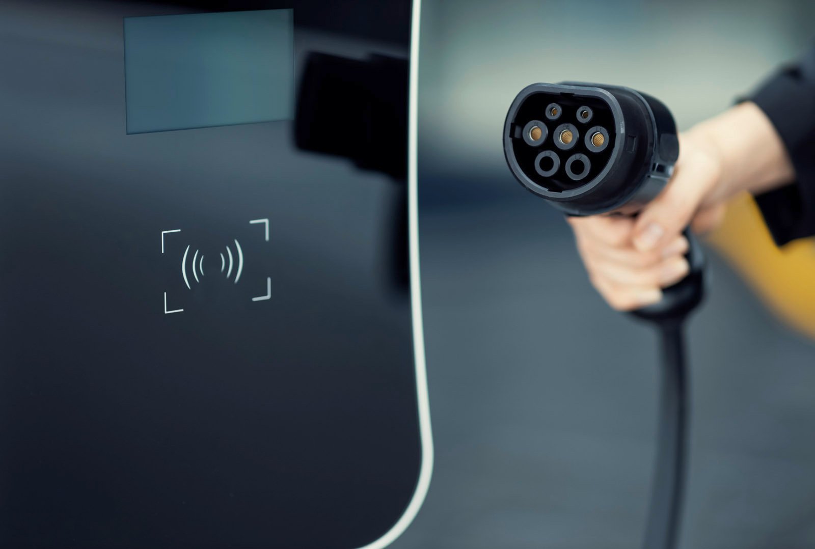 Nahaufnahme eines modernen Schnellladegeräts mit RFID-Leser und einer Hand, die ein Ladekabel hält – Symbol für DC-Ladelösungen im Autohaus