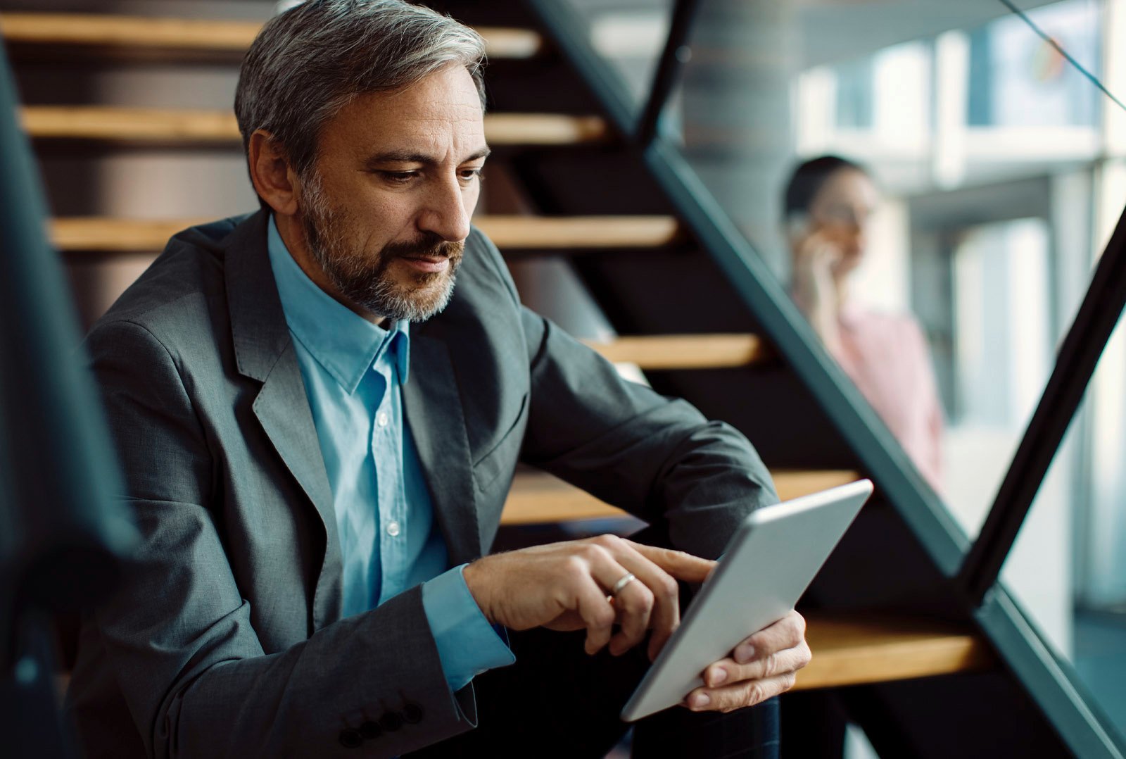 Geschäftsmann in grauem Anzug nutzt ein Tablet auf einer Treppe in modernem Büro – steht für digitale Cross-Selling-Automation und Effizienzsteigerung