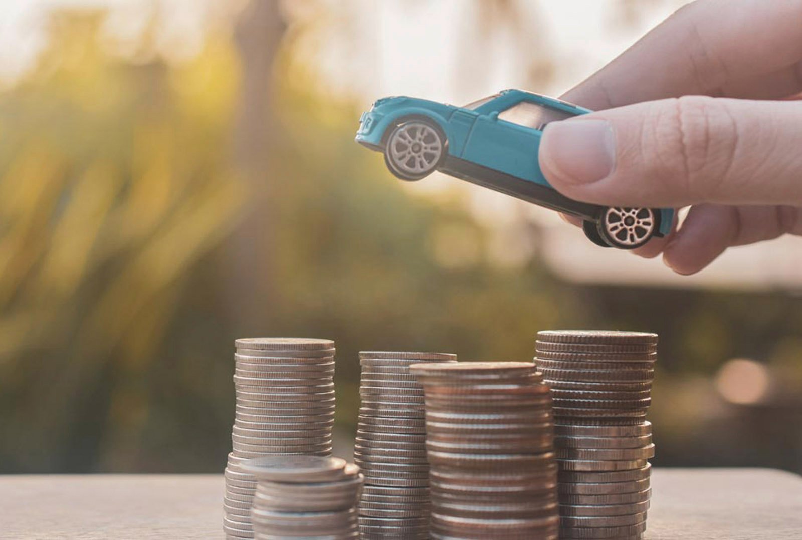 Hand platziert ein blaues Spielzeugauto auf Münzstapel – symbolisiert finanzielle Vorteile durch die THG-Prämie im Bereich Elektromobilität
