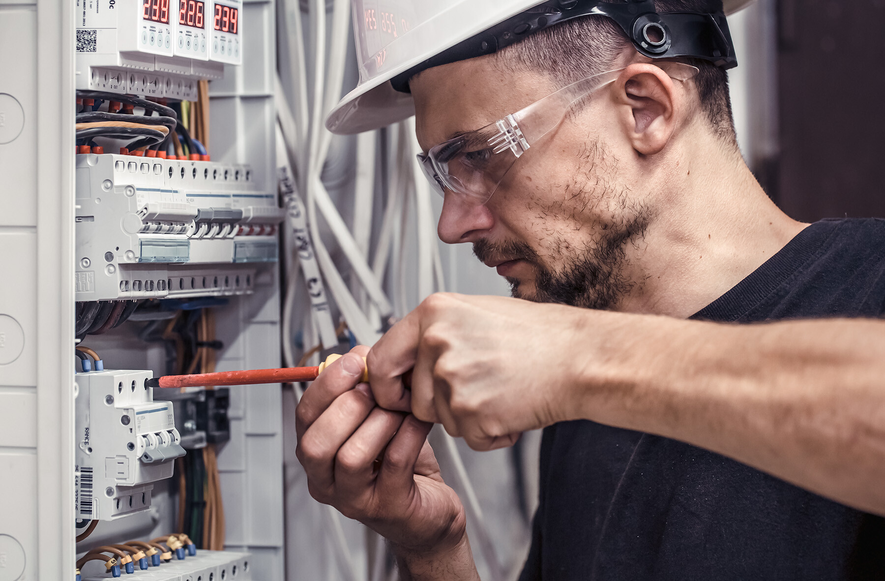 Elektriker mit Schutzbrille und Helm arbeitet an einem Sicherungskasten – Symbol für professionelle Installation und Wartung von Ladeinfrastruktur im Unternehmensumfeld